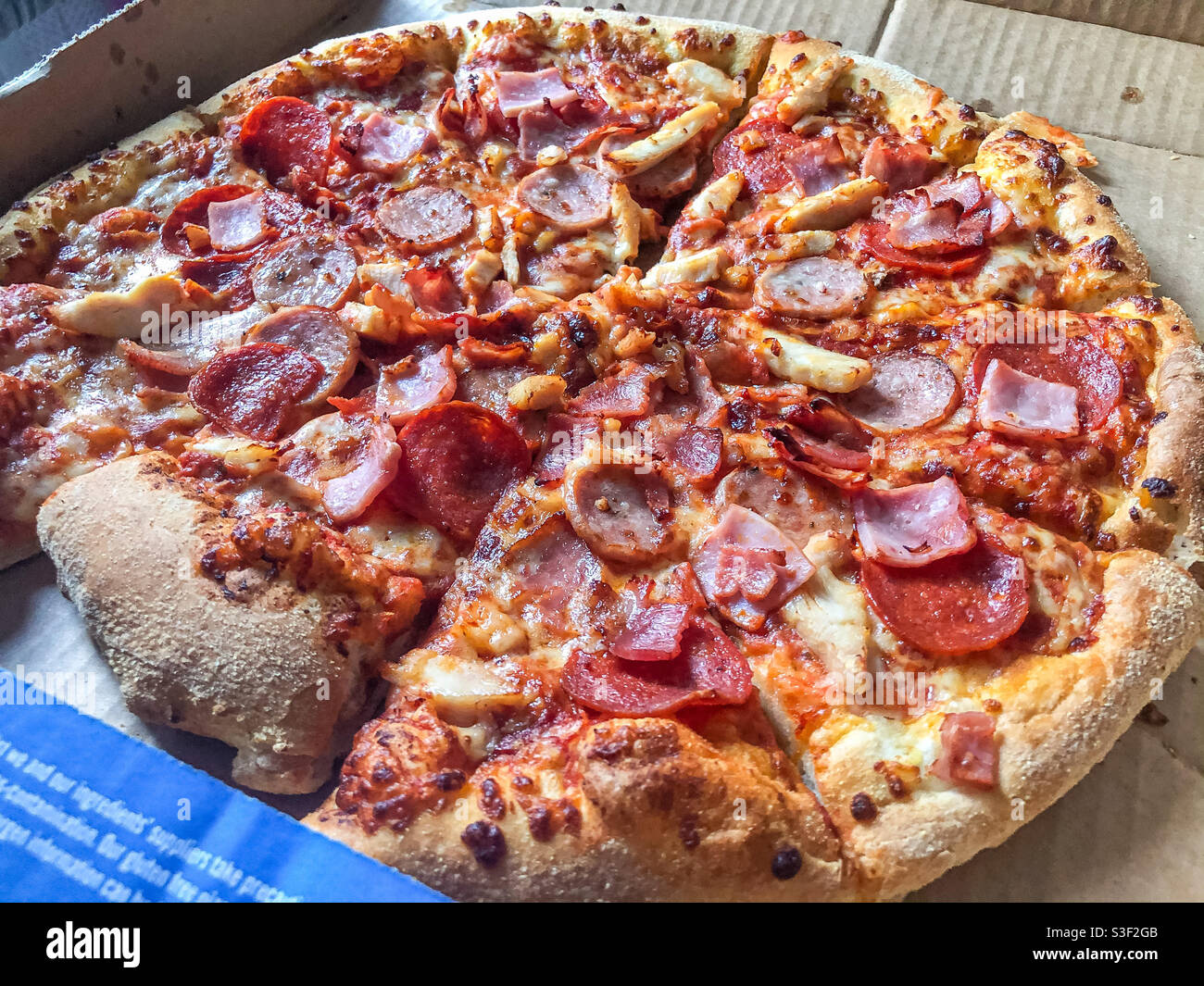 Nahaufnahme einer Pizza zum Mitnehmen mit Speck, Schinken, Käse, Tomaten und Pepperoni zum Beladen Stockfoto
