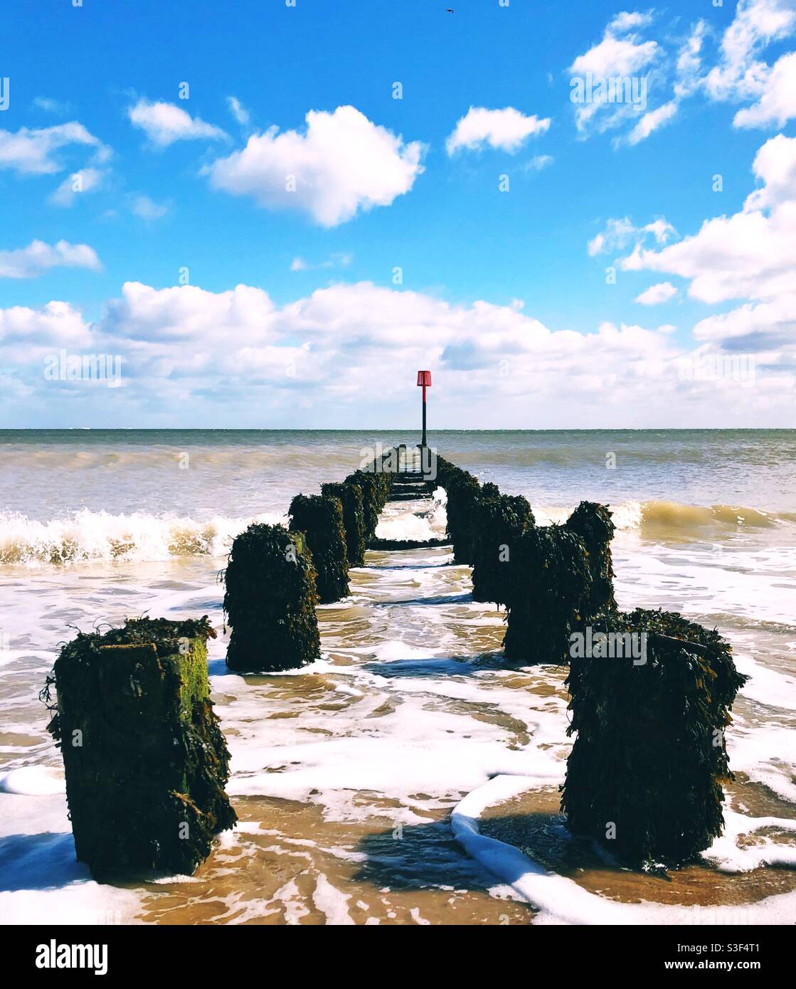 Holzsäulen, die sich an der englischen Küste bis ins Meer erstrecken Unter einem blauen Himmel - Smartphone-aufgenommenes Stockfoto