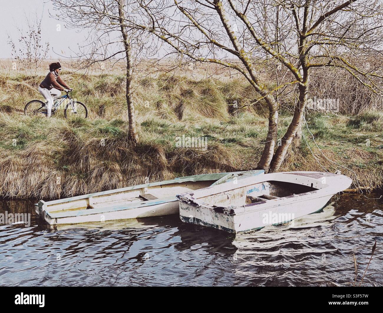 Frau, die mit zwei Booten auf einem an einen Kanal angrenzenden Wanderweg in Carnon Plage, in der Nähe von Montpellier, Südfrankreich, radeln muss Stockfoto