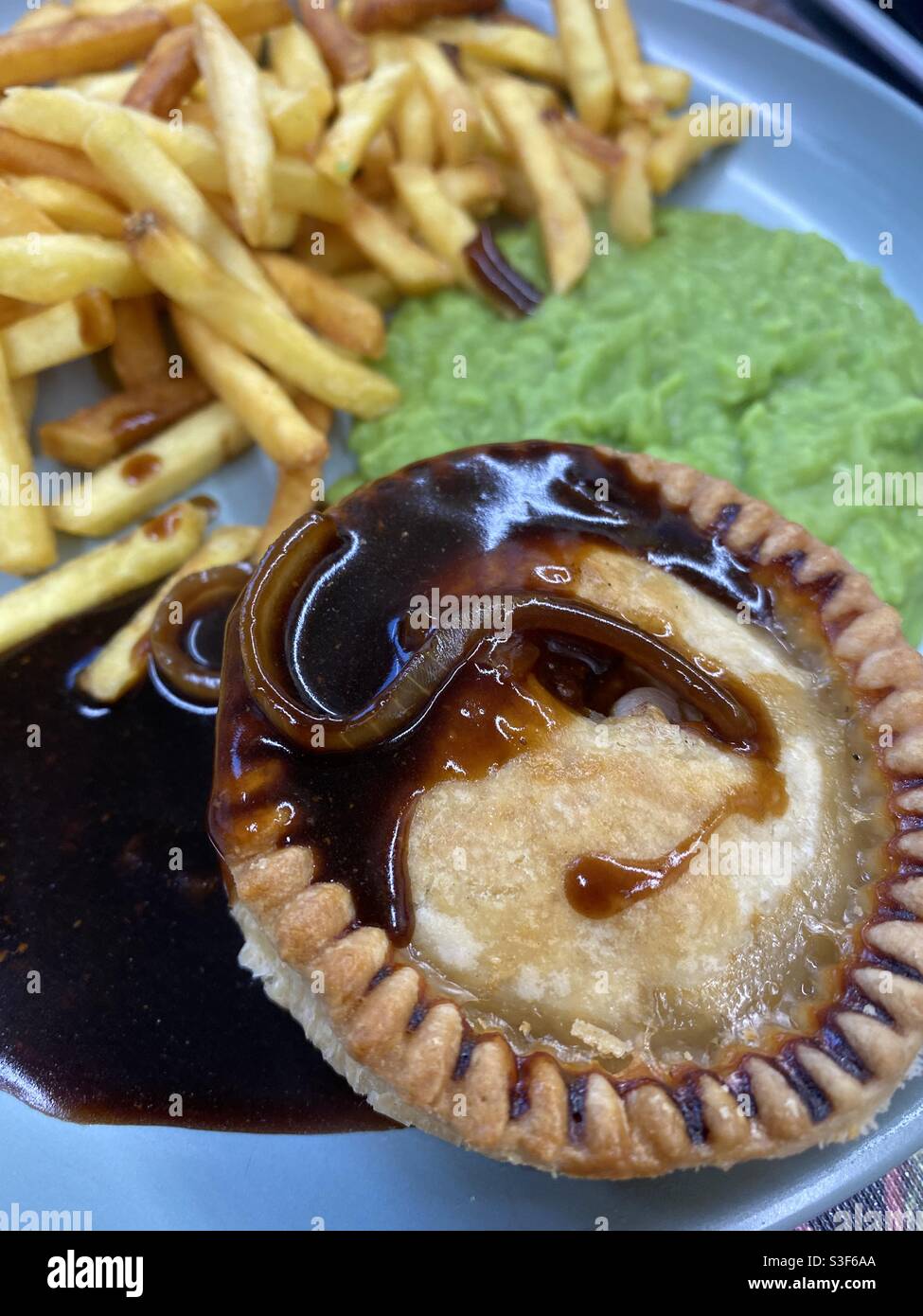 Pie, Zwiebelsoße, Pommes und matschige Erbsen - Smartphone-aufgenommenes Stockfoto