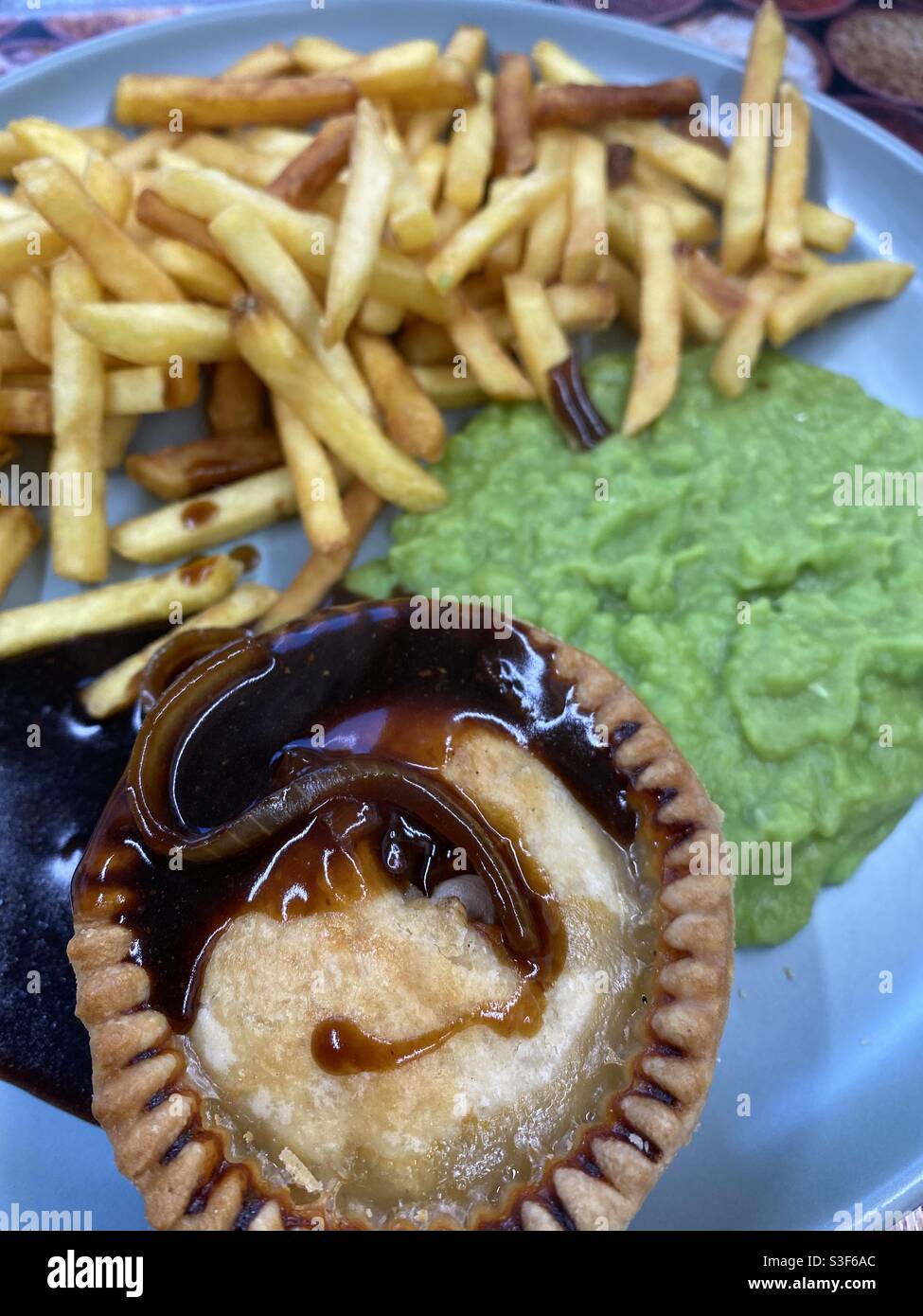 Pie, Zwiebelsoße, Pommes und matschige Erbsen - Smartphone-aufgenommenes Stockfoto