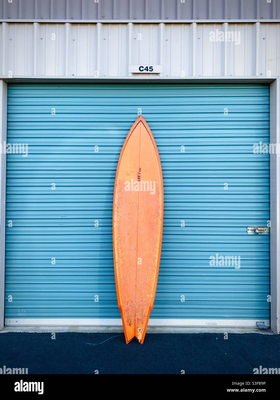 Ein orangefarbenes Surfbrett gegen eine Garage. Stockfoto