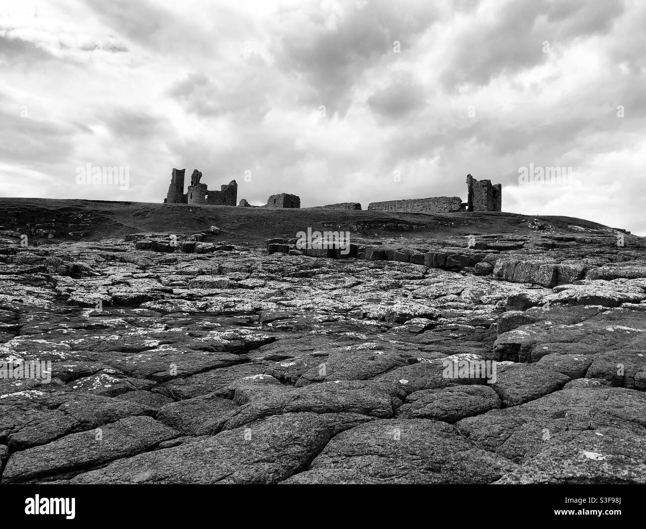 Dunstanburgh Castle. Blick über die felsige Küste zum Schloss. Ein Schwarzweißfoto Stockfoto