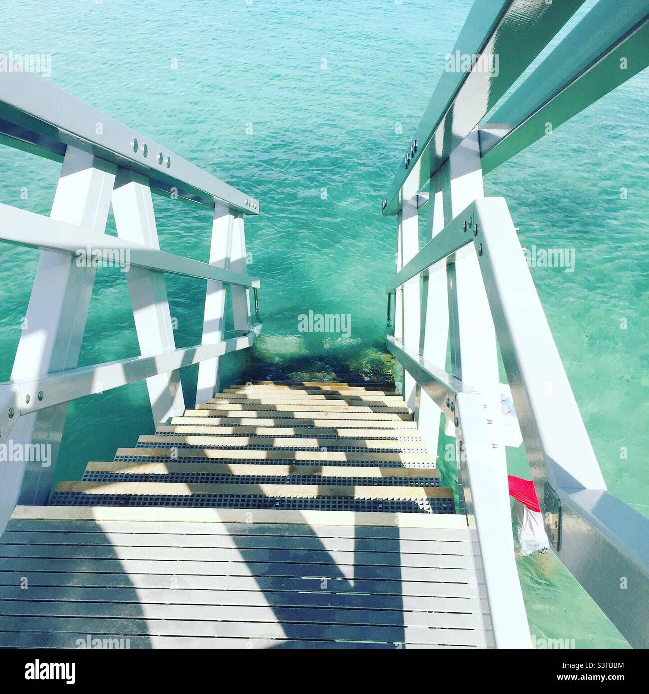 Weiße Treppen führen hinunter zu kristallklarem, türkisfarbenem Wasser. Stockfoto