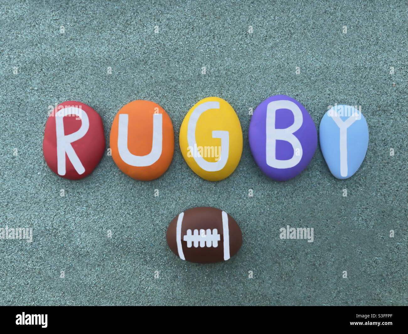 Rugby, Sportname mit handgefertigten mehrfarbigen Steinbuchstaben über grünem Sand Stockfoto