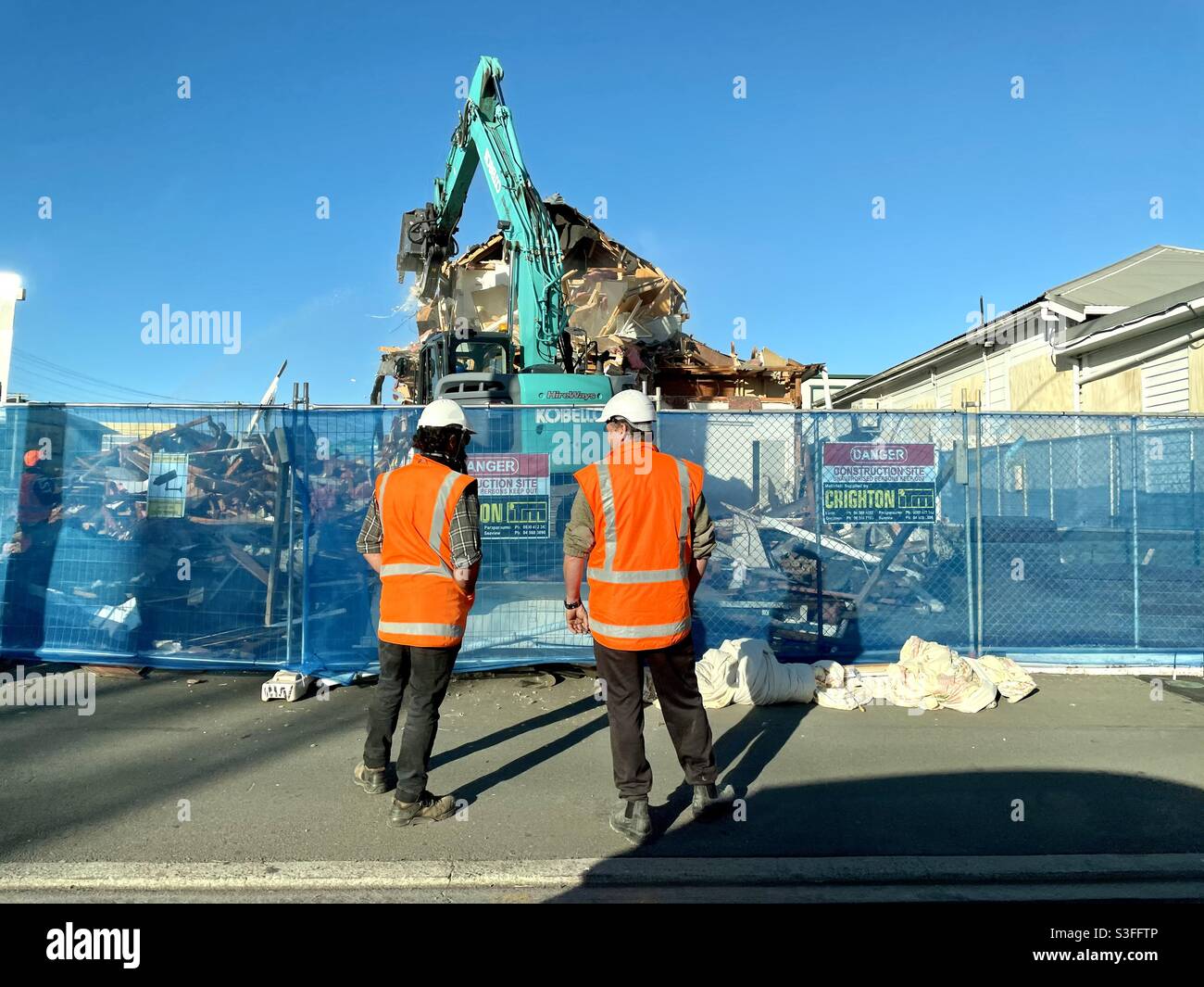 Arbeiter in Unterhemden beobachten den Abriss eines Gebäudes in Wellington, Neuseeland. Es wird durch einen Apartmentblock mit mittlerer Dichte ersetzt. - Smartphone-aufgenommenes Stockfoto