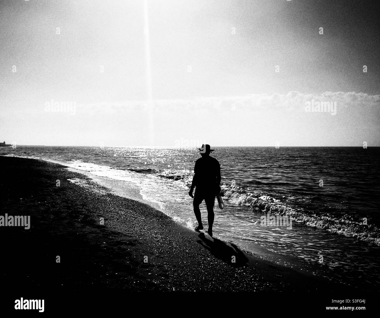 Silhouette eines Mannes im Hut, der am Meer entlang geht - Smartphone-aufgenommenes Stockfoto