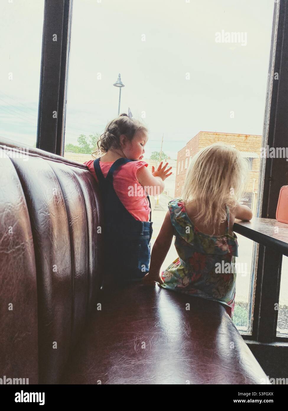 Zwei kleine Mädchen, die in einem Restaurantstand sitzen und aus dem Fenster schauen. Stockfoto