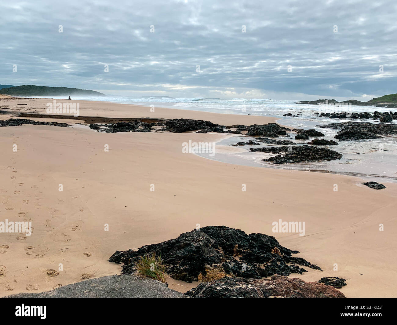 Wolkiger Himmel, wirbelndes Wasser der Felsenpools, die sich um die Felsen und den Sand drehen, sawtell Beach, Australien, Herbst Stockfoto