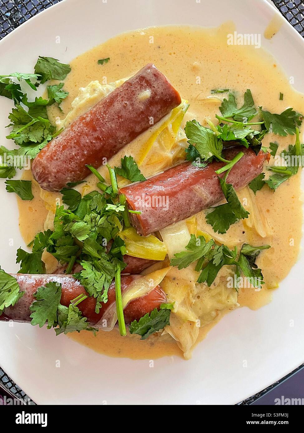 Flache Laie einer Gourmet-Würstchen und Lauch in einer Senf-Sahnesauce garniert mit Koriander - Smartphone-aufgenommenes Stockfoto