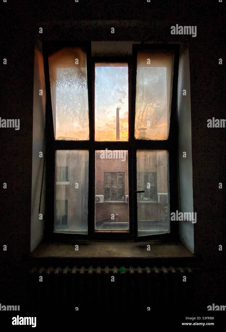 Altes, dreckiges Fenster mit Sonnenuntergangshimmel und Fabrikrohr Stockfoto