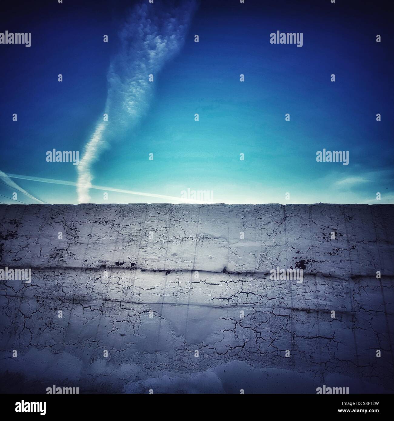 Ein abstraktes Foto einer industriellen, weiß gestrichenen Wand mit Himmel und Kondensstreifen dahinter. Speicherplatz kopieren - Smartphone-aufgenommenes Stockfoto