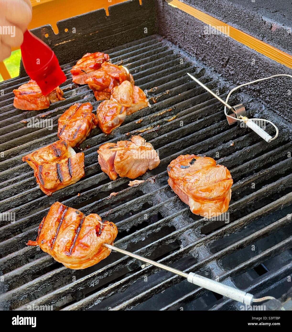 Mann, der Schweinemedaillons auf seinem Hinterhofgrill grillt und die Temperatur mit einer elektrischen Sonde misst, USA - Smartphone-aufgenommenes Stockfoto
