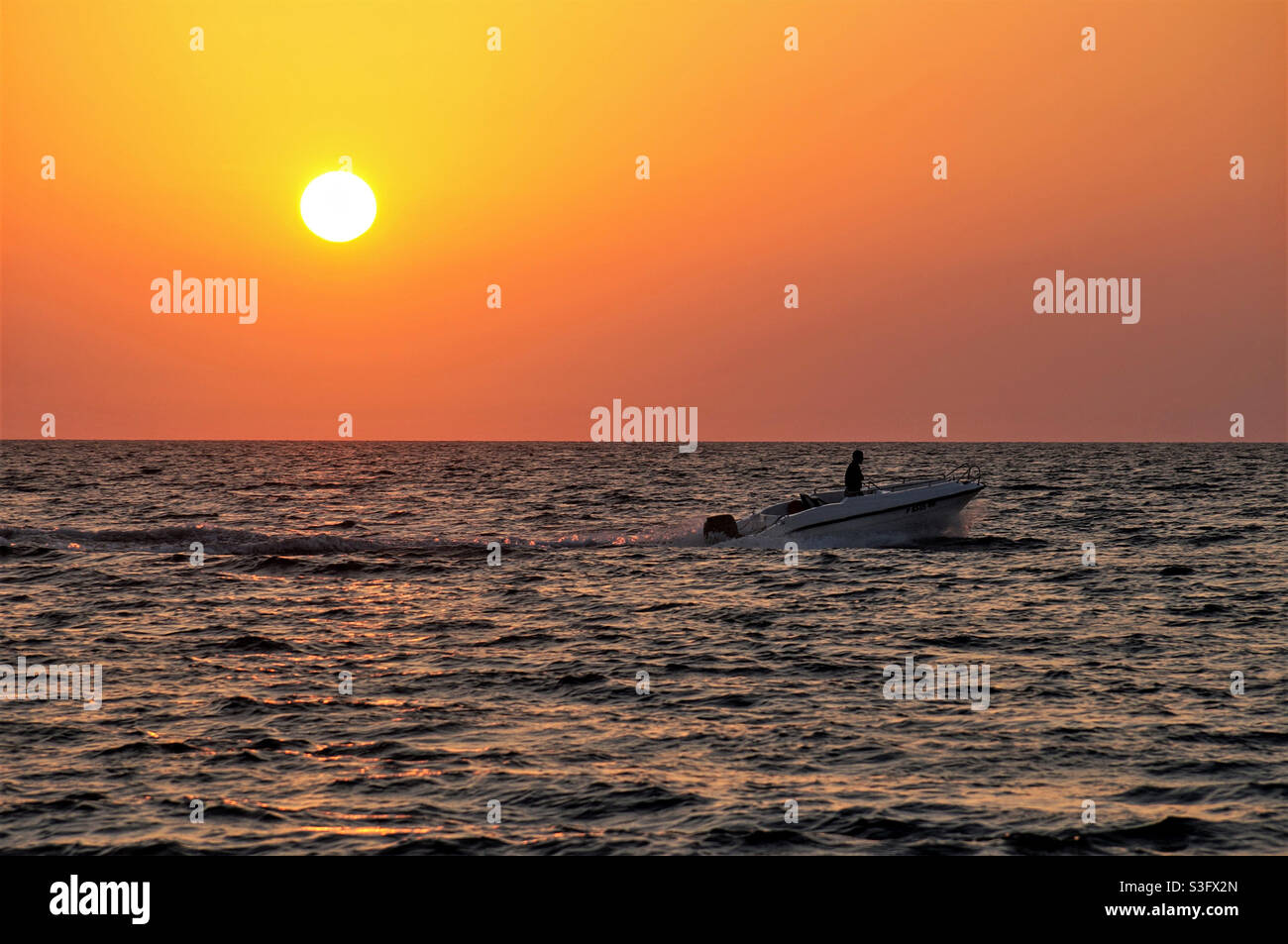 Silhouette eines Mannes auf einem Boot, der bei Sonnenuntergang auf dem Meer segelt Stockfoto