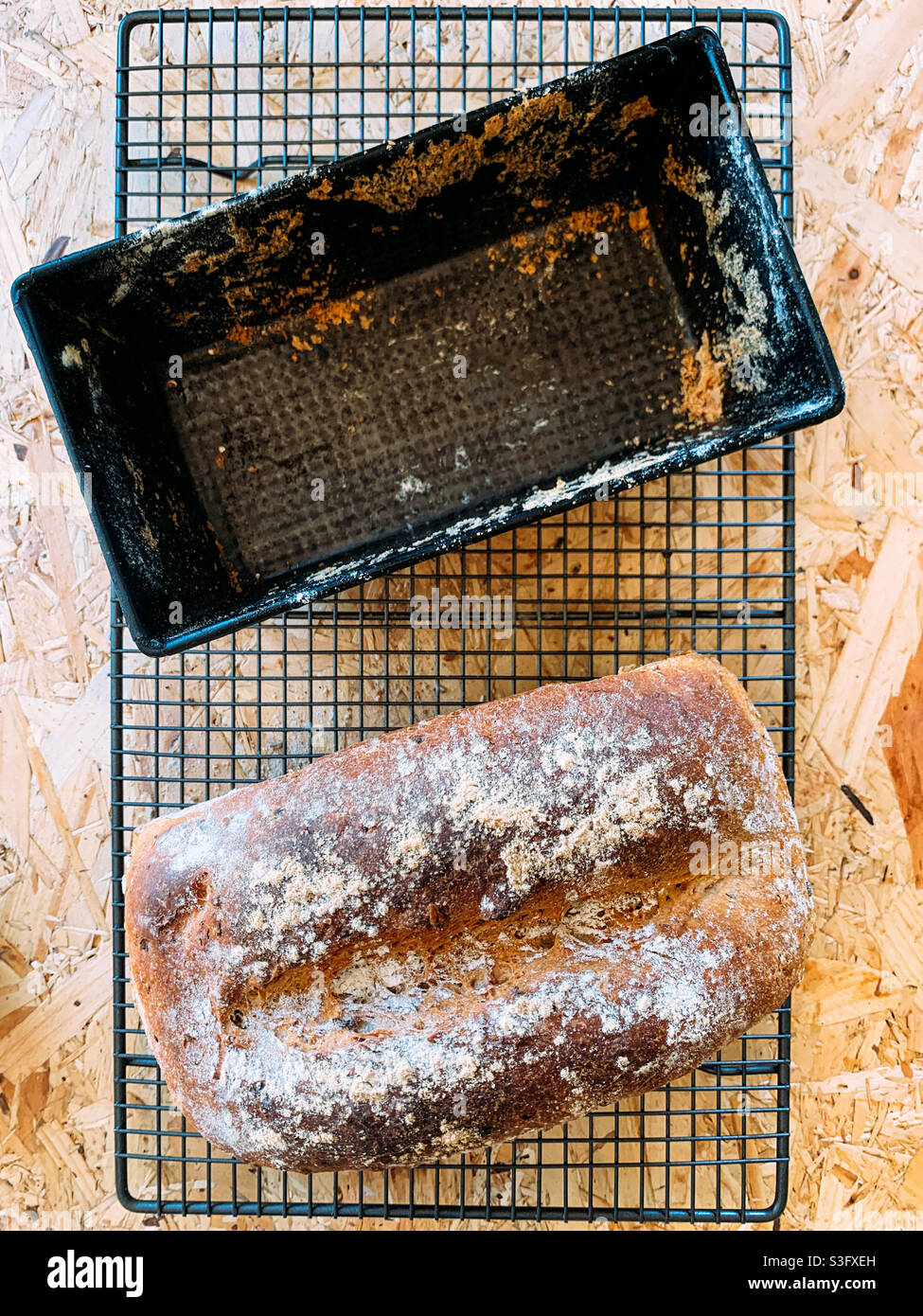 Draufsicht auf ein selbstgebackenes Getreidebrot und eine leere Brotdose auf einem Holzhintergrund - Smartphone-aufgenommenes Stockfoto