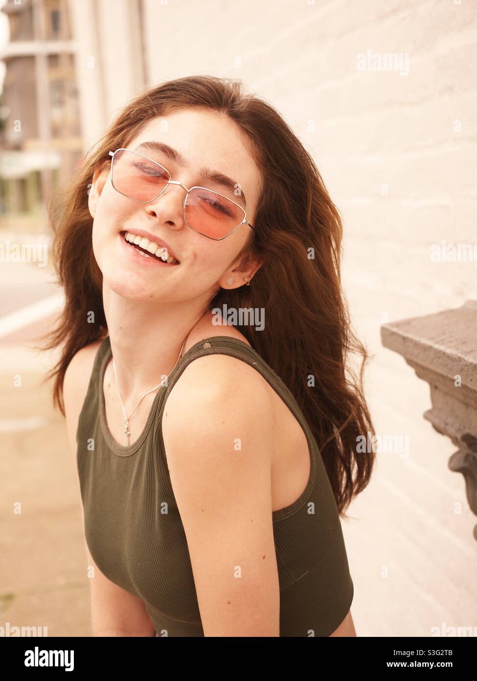 Portrait, hübsche junge Frau lächelnd, Brünette mit langen Haaren und Sonnenbrille Stockfoto