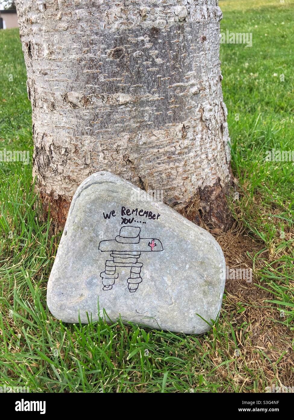 Ein bemalter Inukshuk, der auf einem Felsen neben einem Baum gemalt wurde. Stockfoto