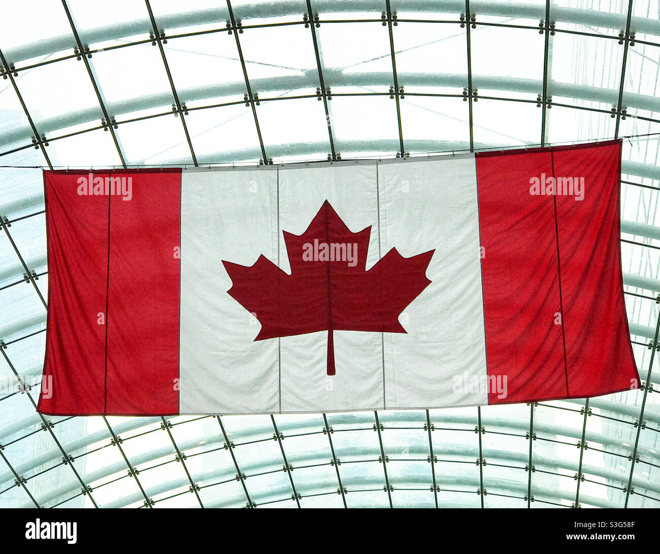 Die rot-weiße kanadische Ahornblattflagge, die an der Glasdecke eines Gebäudes hängt. Stockfoto