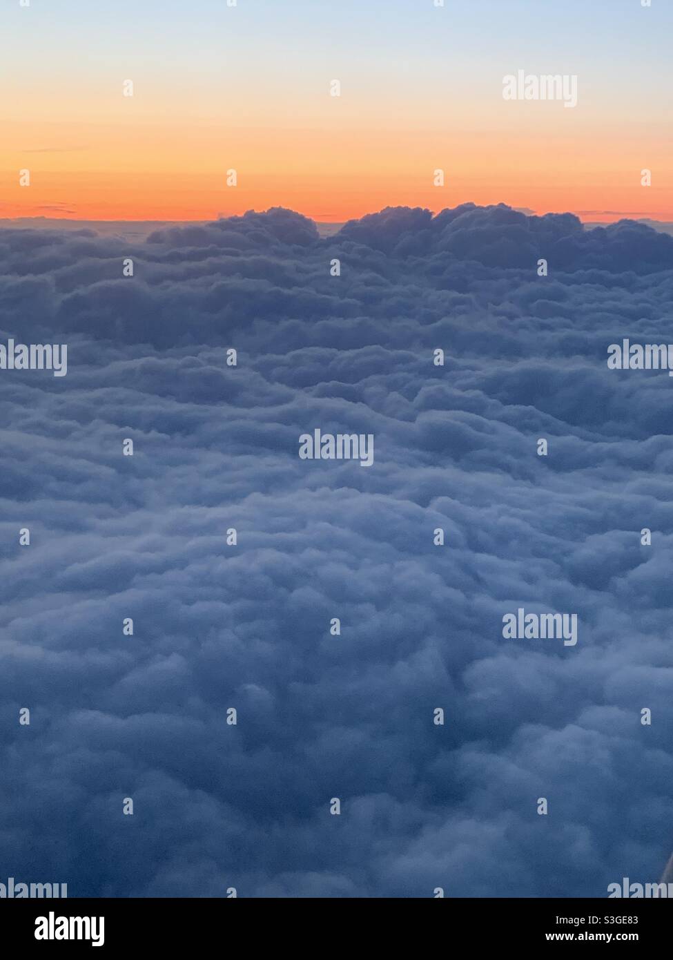 Sonnenuntergang aus einem Flugzeug mit Wolken vor sich Rollen und einem orangen Himmel in der Ferne. Stockfoto