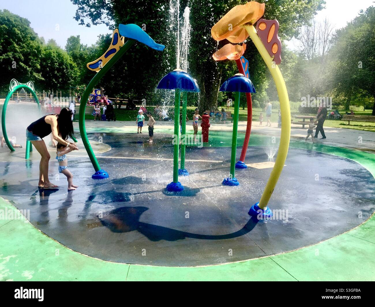 Mama und Kröte in einem wässrigen Wunderland an einem warmen Sommertag, Ontario, Kanada. Wasser kaskadieren, sprühen, spritzen. Wasserspaß für alle. - Smartphone-aufgenommenes Stockfoto