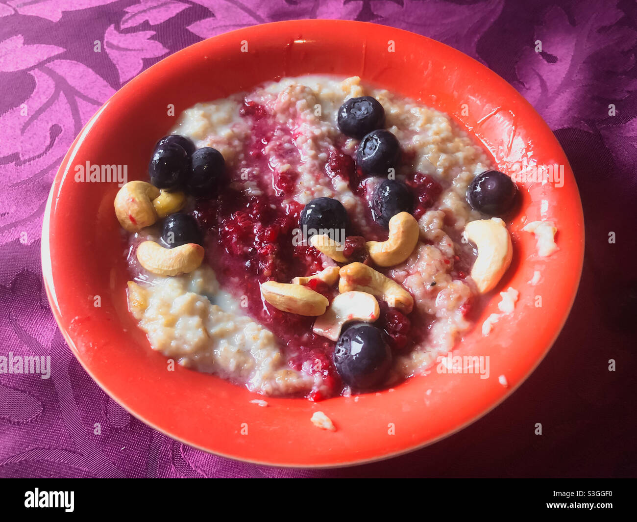 Eine Schüssel Haferbrei mit Hafer und Milch mit Himbeeren, Heidelbeeren und Cashewnüssen zum Frühstück. Stockfoto