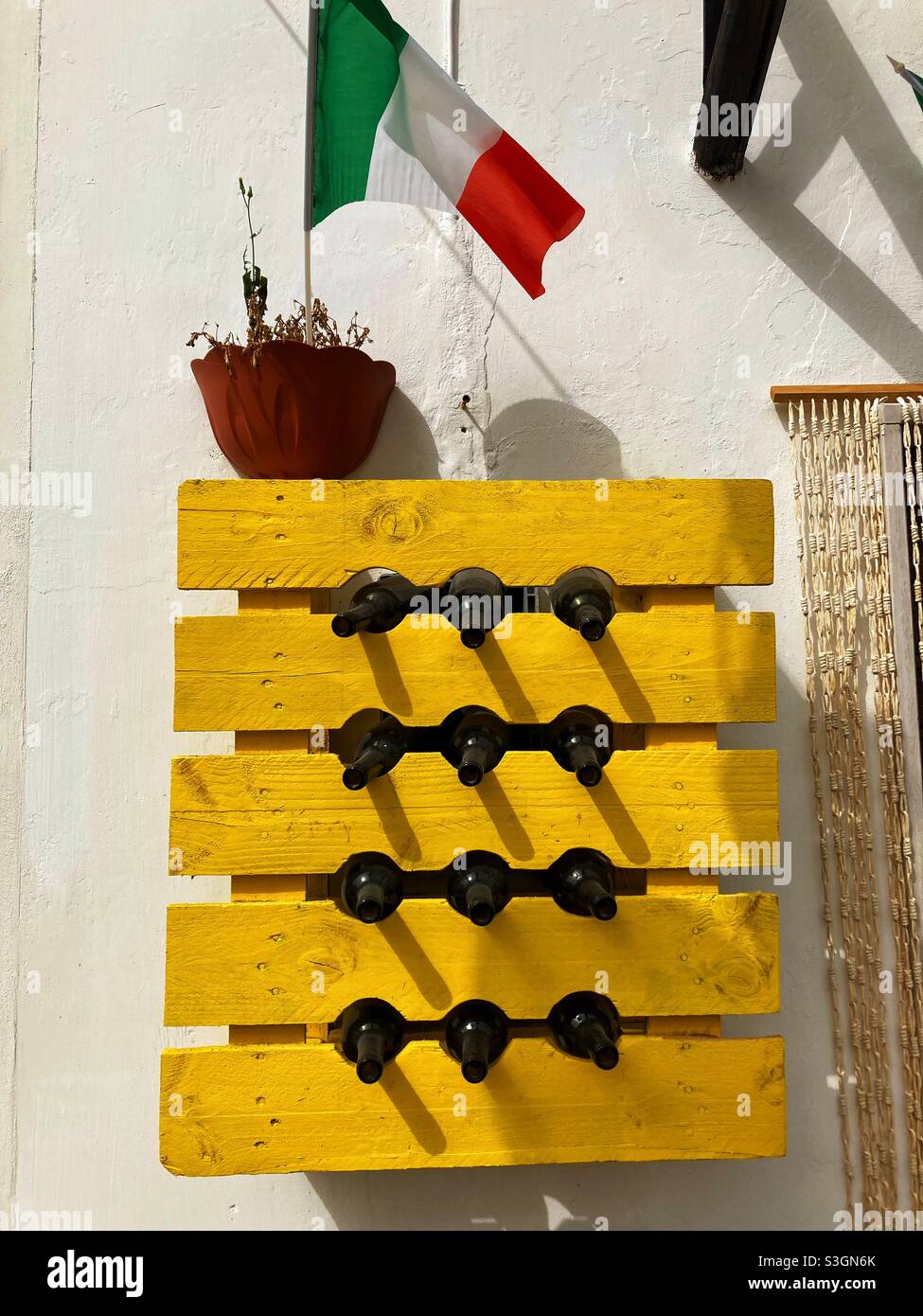 Ein leuchtend gelbes Weinregal, gefüllt mit neun leeren Weinflaschen an einer Wand eines Restaurants in der Stadt Vieste, Gargano, Apulien, Italien Stockfoto