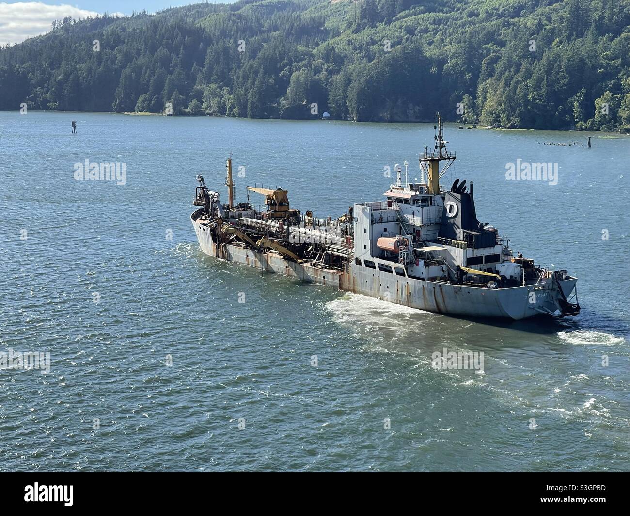 Draggerschiff auf dem Columbia River, das vom Hafen von Portland, USA, zum Pazifischen Ozean fährt. Auf dem Hintergrund ist dichter Nadelwald. Stockfoto