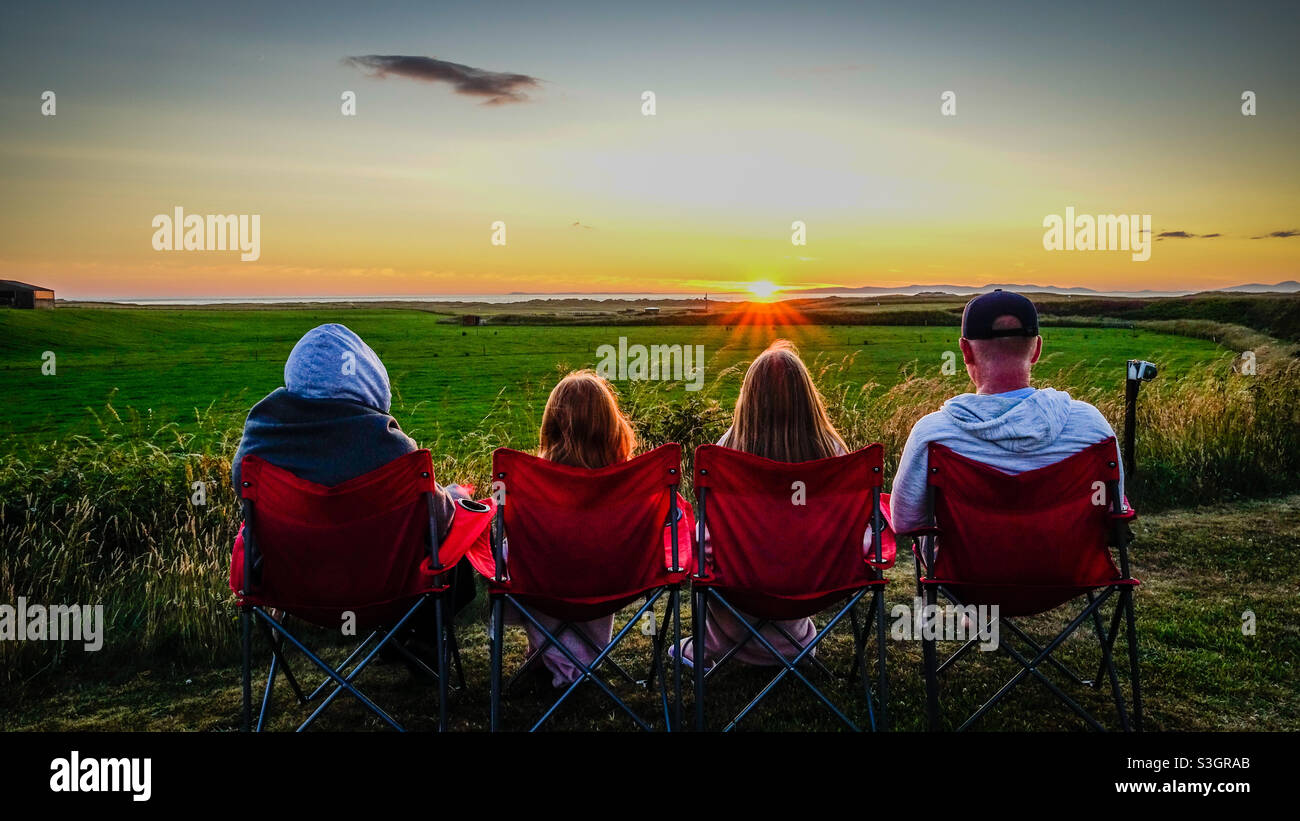 Vierköpfige Familie beobachtet den Sonnenuntergang über Islay von Machrihanish in Kintyre in Schottland Stockfoto