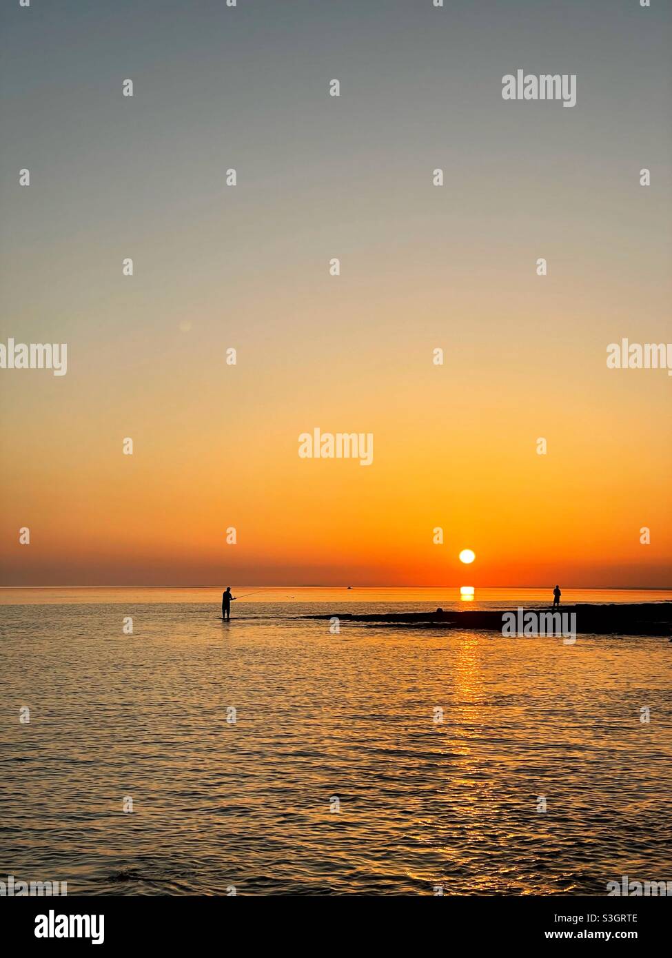 Seeangler an der Küste von Südwales bei Sonnenuntergang, Juli. Stockfoto