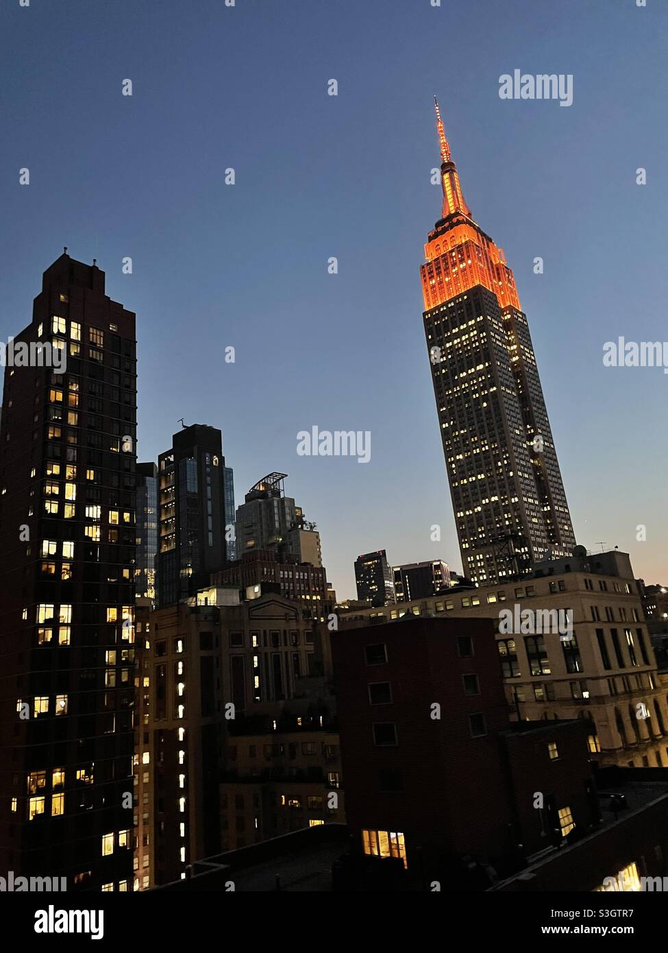 Empire State Building im Abendlicht mit orangefarbener Lichtanzeige. - Smartphone-aufgenommenes Stockfoto