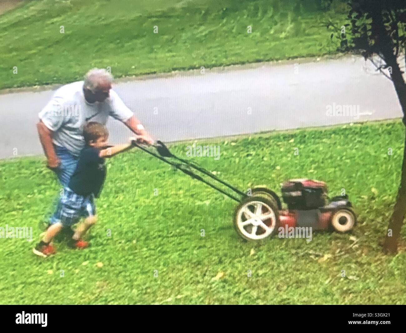 Junge schneidet Gras mit Großvater Stockfoto