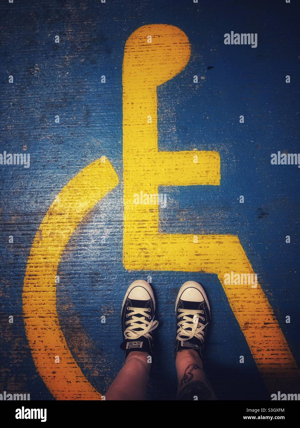 Ich trug Converse und stand auf einem gemalten Behindertenschild auf dem Boden eines Parkplatzes Stockfoto
