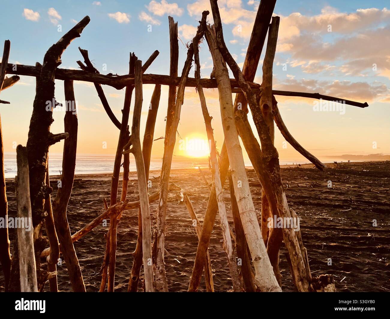 Die untergehende Sonne wird durch ein Tipi aus Treibholz am Castlecliff Beach in der Nähe von Whanganui in Neuseeland gesehen Stockfoto