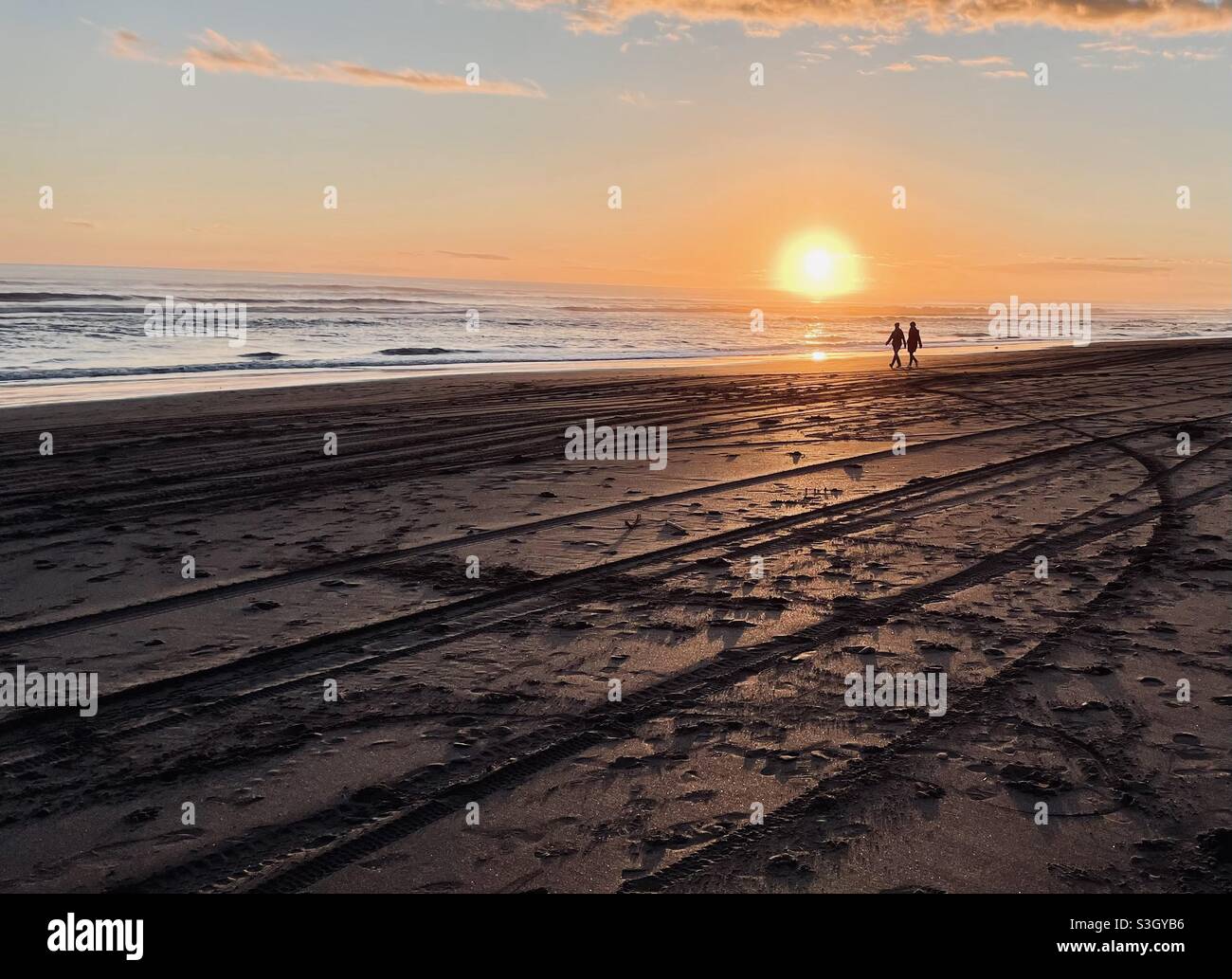 Castlecliff Beach, Whanganui, Neuseeland: Zwei Frauen laufen an einem Winterabend bei Sonnenuntergang am Strand entlang Stockfoto