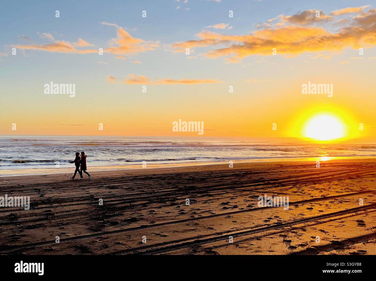 Castlecliff Beach, Whanganui Neuseeland: Zwei Frauen laufen an einem sonnigen Winterabend bei Sonnenuntergang am Strand entlang Stockfoto