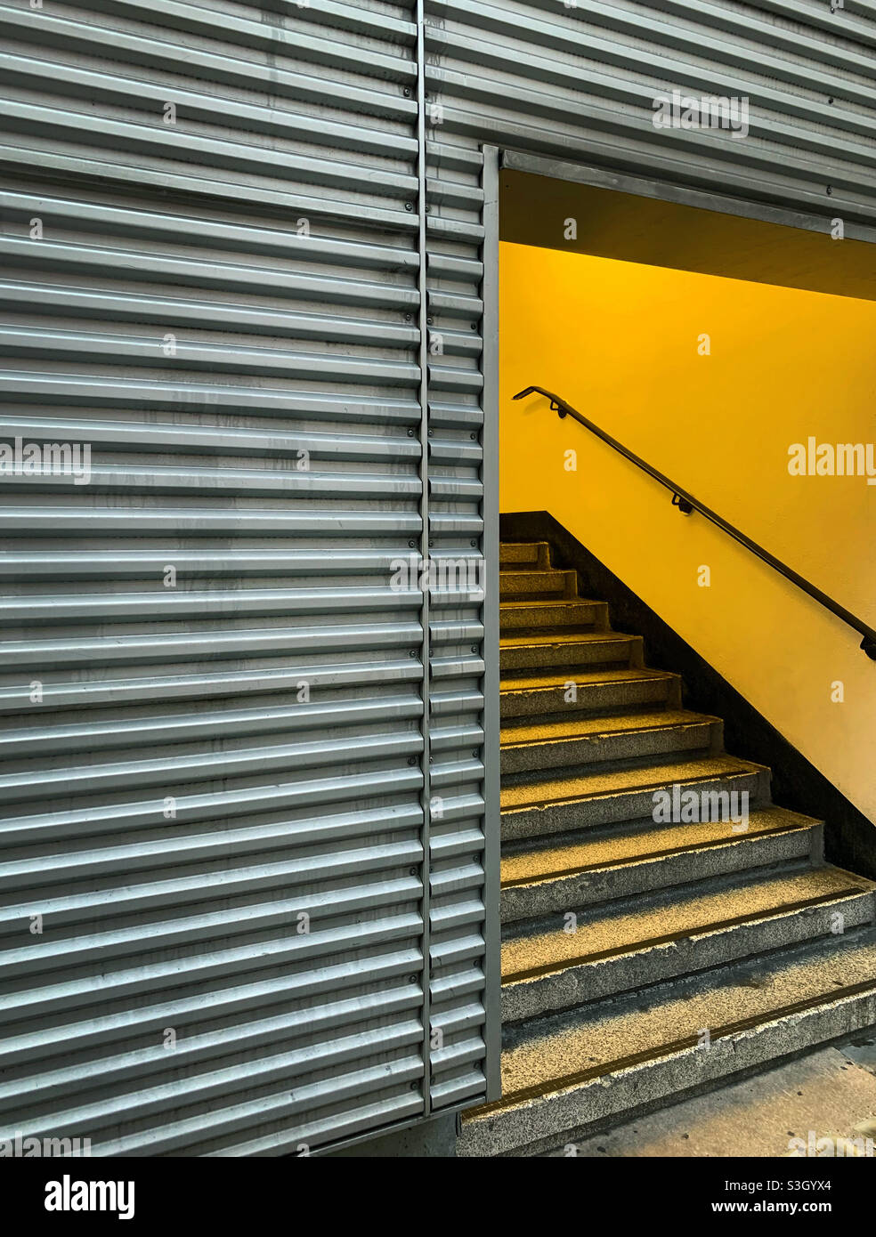 Eine in gelbes Licht getauchte Treppe, die aus EINEM metallverkleideten Gebäude auftaucht Stockfoto