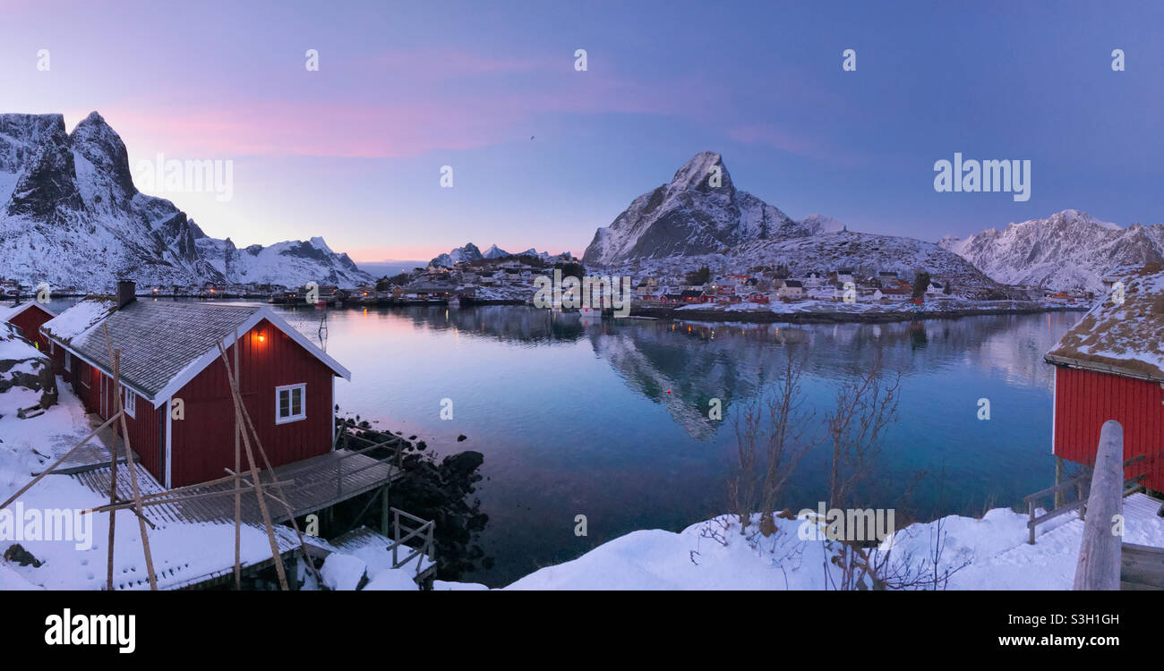 Schönes Fischerdorf reine im Winter, Lofoten-Inseln, Norwegen. Farbenfroher Sonnenuntergang über dem schönen Fischerdorf reine, umgeben von schneebedeckten Fjorden. Stockfoto