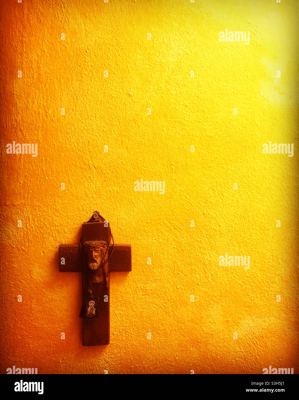 Ein hölzernes Kruzifix mit dem Gesicht Jesu Christi auf einer gelben Wand in Peña de Bernal, Queretaro, Mexiko Stockfoto