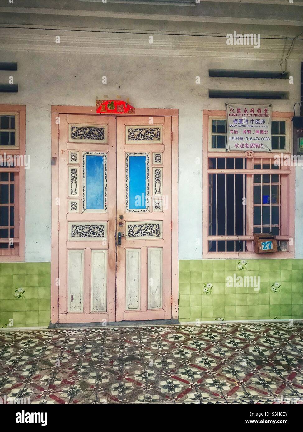 Eine farbenfrohe Tür und gemusterte Fliesen sind Merkmale eines historischen Gebäudes in George Town, Penang, Malaysia - Smartphone-aufgenommenes Stockfoto