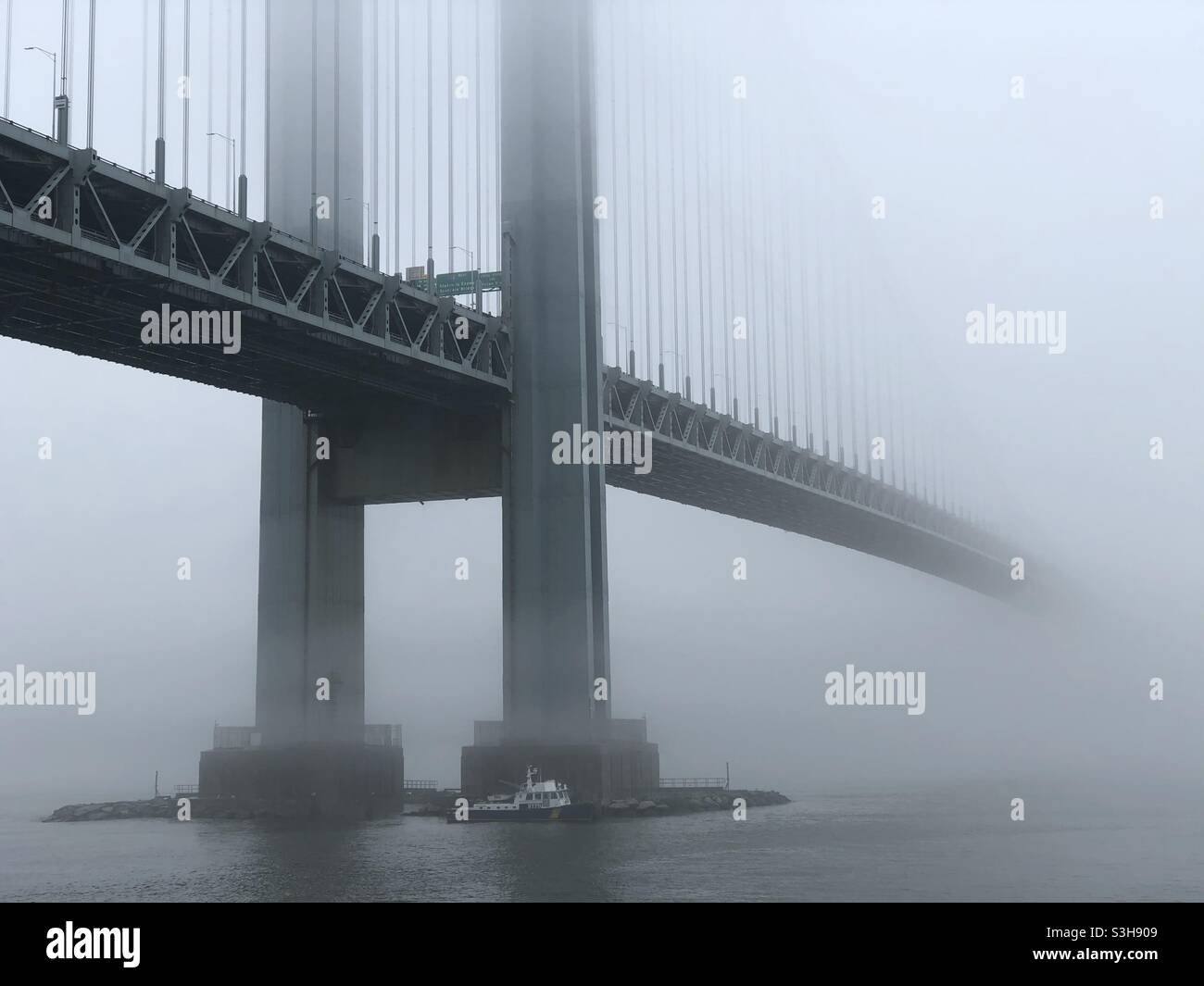 Verrazzano-Narrows Brücke im Nebel. Ein NYPD-Patrouillenboot schwimmt in der Nähe der Brooklyn-Seite der Brücke. Stockfoto