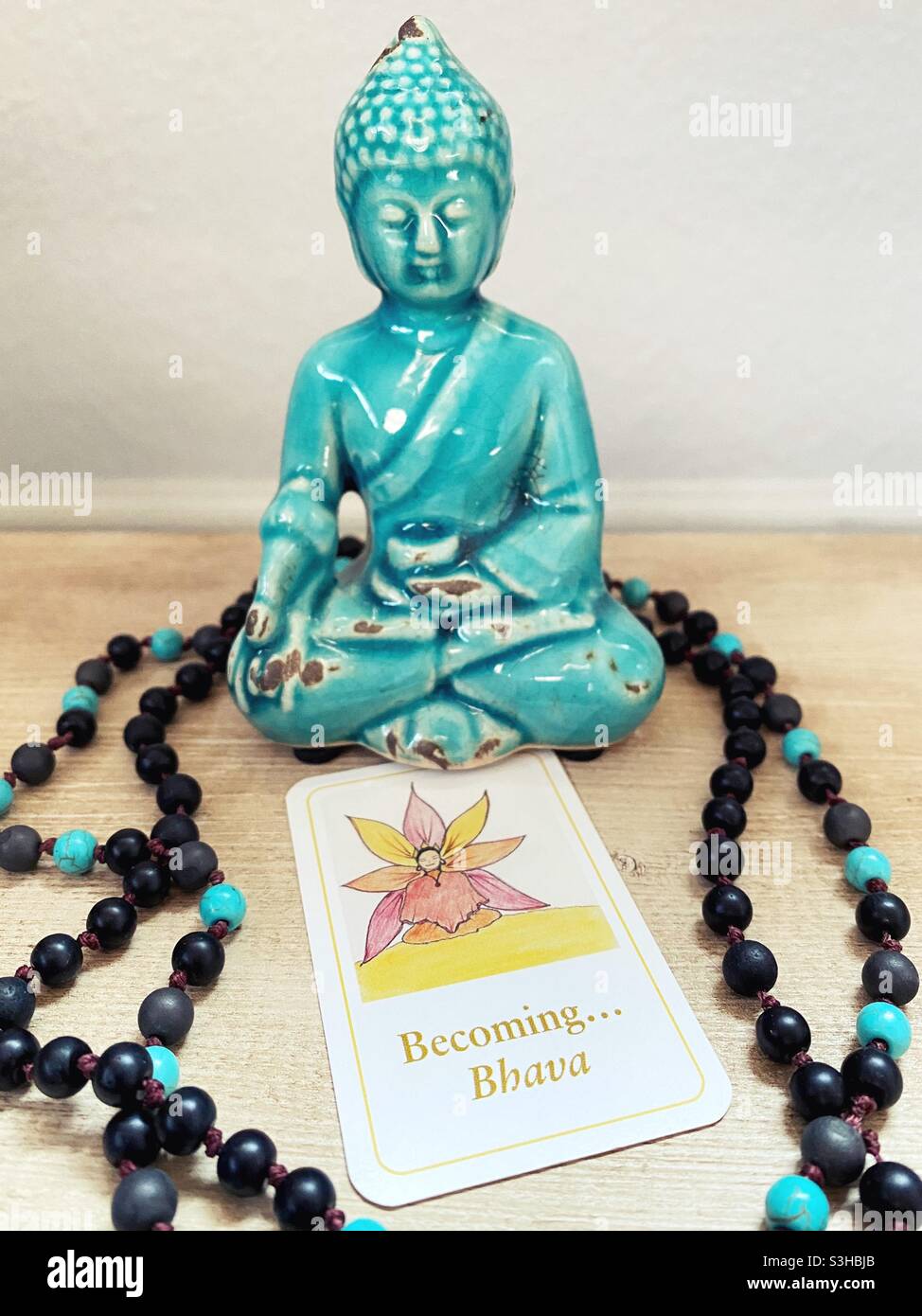 Eine Buddha-Figur, Gebetsperlen und eine umgedrehte Dharma-Karte mit dem Wort „Werden“. Stockfoto