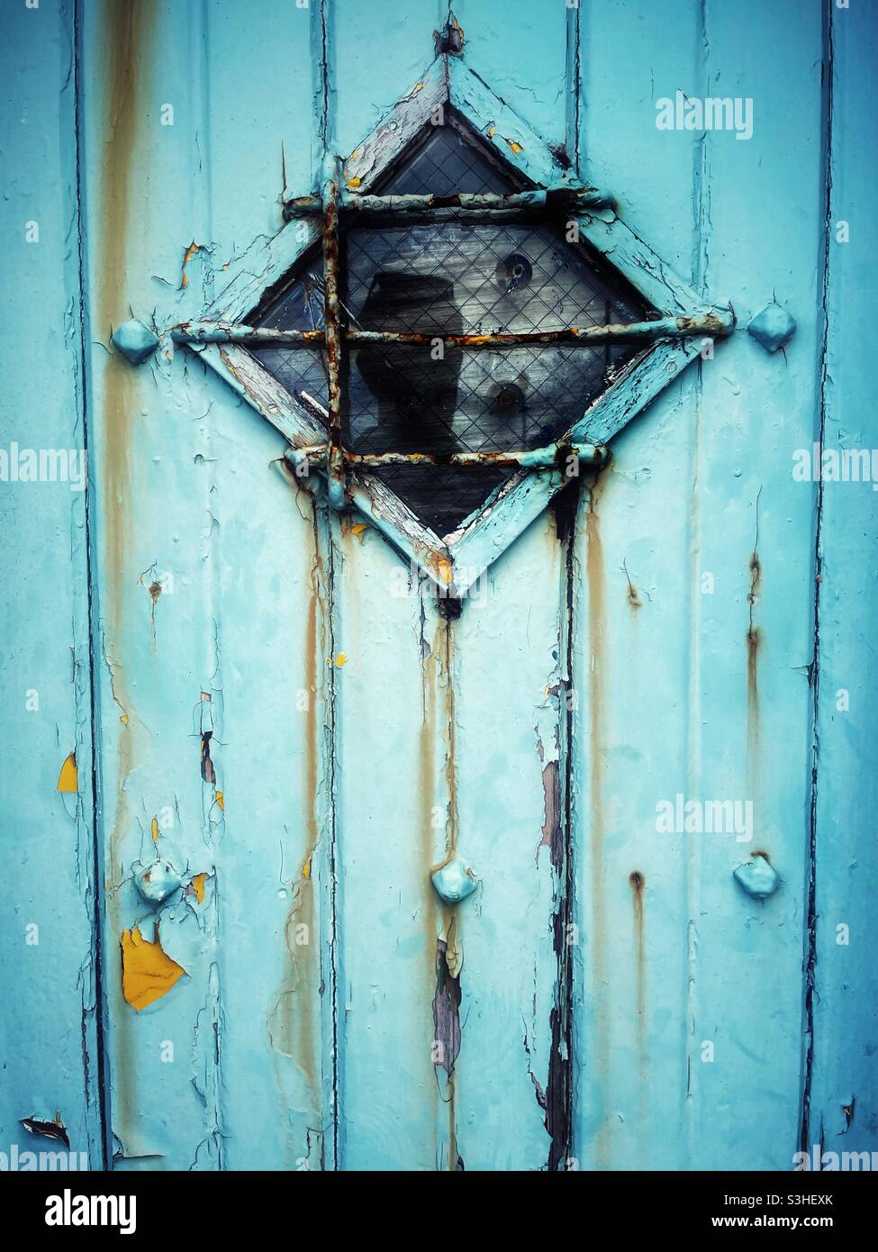 Alte, verwitterte blaue Tür mit Diamantfenster. Stockfoto