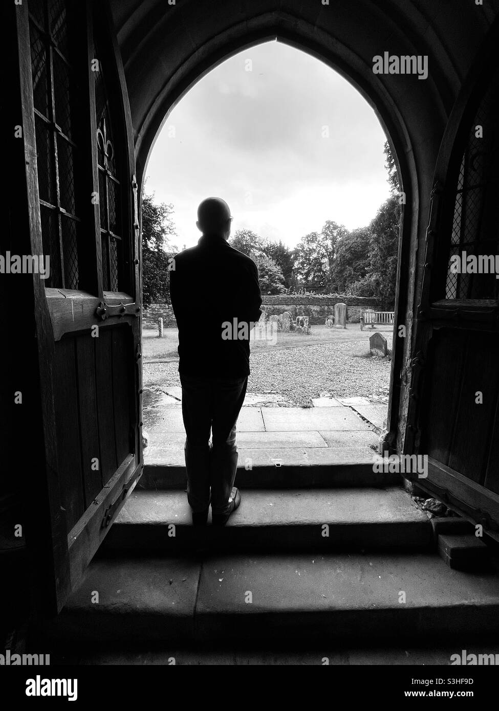 Ein Mann beobachtet den Regen durch eine offene Kirchentür. Oxfordshire, Großbritannien. Stockfoto