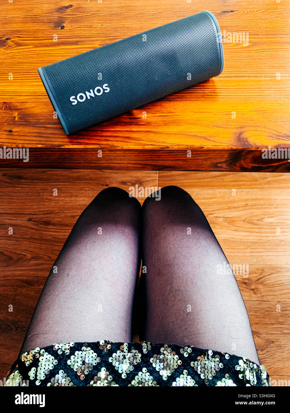 Sonos Roam tragbaren Lautsprecher auf einem Holztisch neben einer Frau, die ein Paillettenkleid trägt Stockfoto