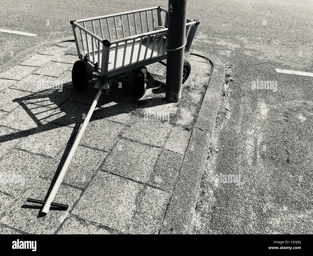 Ein leerer Wagen steht an einem sonnigen Tag auf dem Bürgersteig, der an einen Laternenpfahl gekettet ist Stockfoto