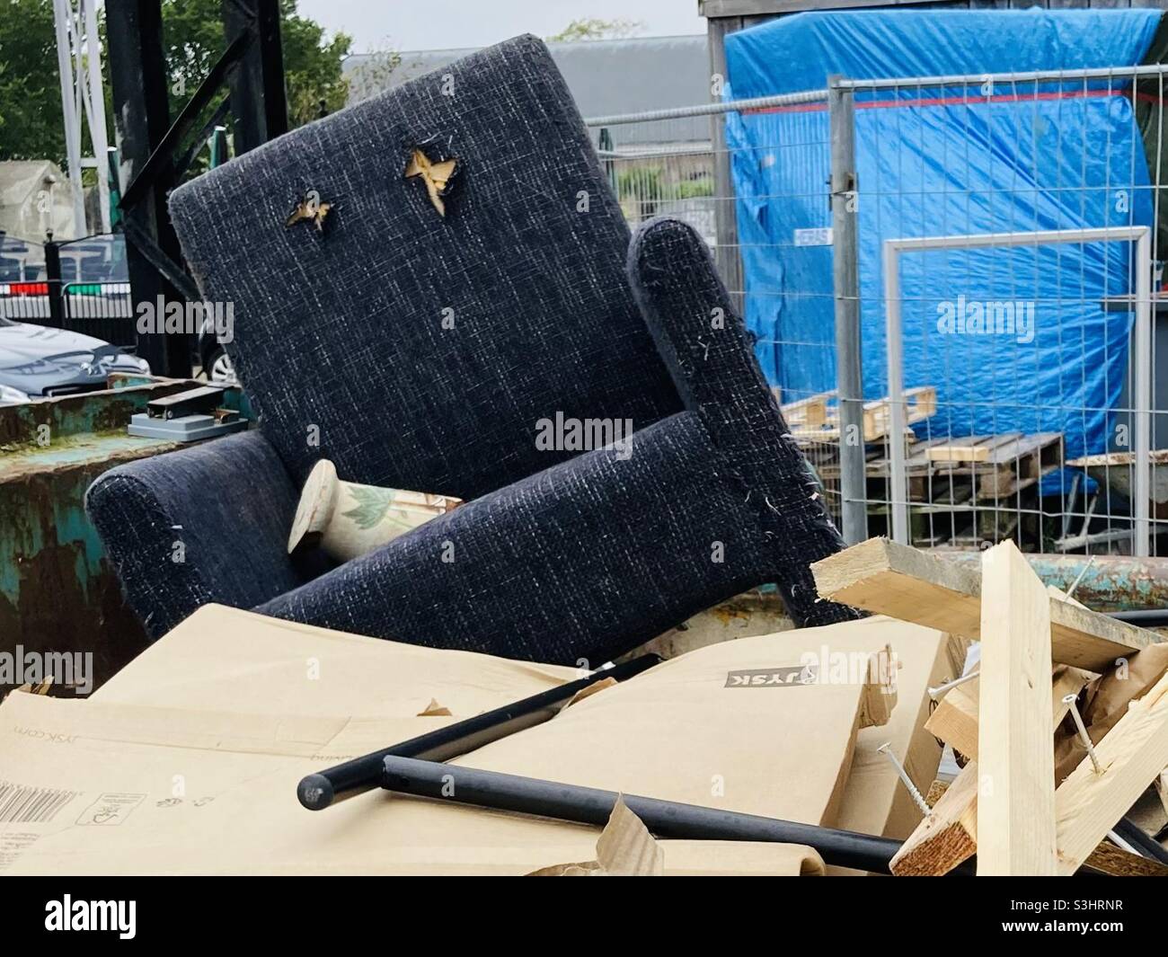 Alter gebrochener blauer Sessel, der mit anderen Abfällen in einem Container liegt - Smartphone-aufgenommenes Stockfoto