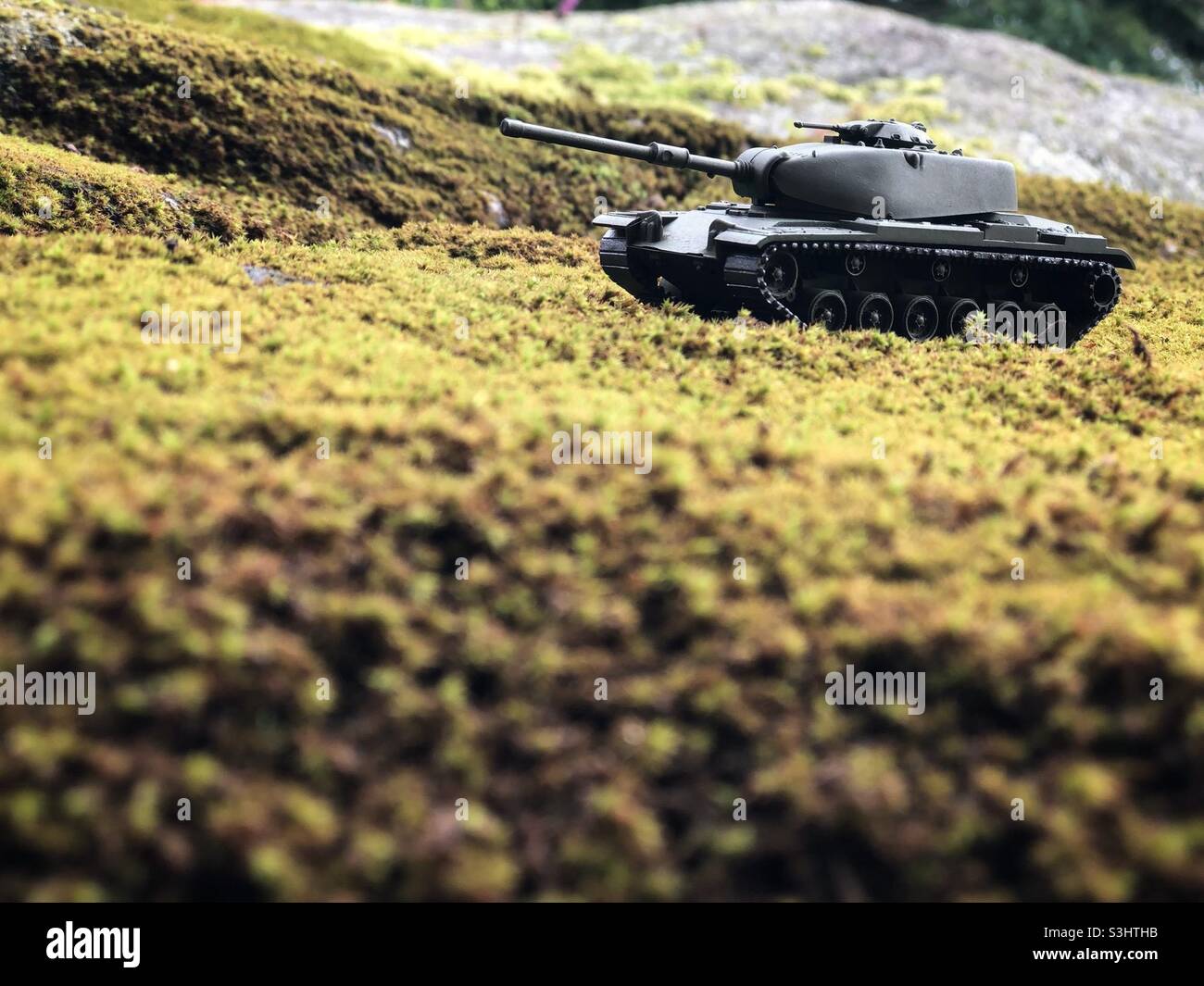 Ein kleiner Panzer der Spielzeugarmee, der auf einem mit Moos bedeckten Felsbrocken aufgestellt ist. Stockfoto