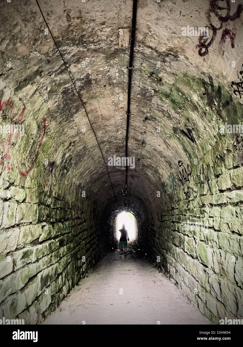 Anonyme Silhouette, die durch ein dunkles, simbolisierendes Licht am Ende des Tunnels unter der Passhöhe geht - Smartphone-aufgenommenes Stockfoto