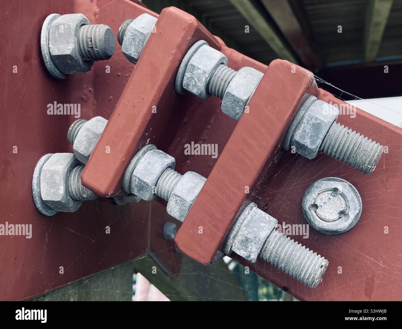 Der rote Metallrahmen wird mit grauen Metallschrauben und Muttern befestigt Stockfoto