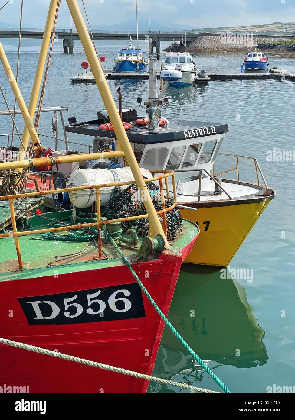 Fischerboote im Hafen von Port Magee, die Brücke zur Insel Valentia ist in der Ferne sichtbar, County Kerry, Irland, August. - Smartphone-aufgenommenes Stockfoto